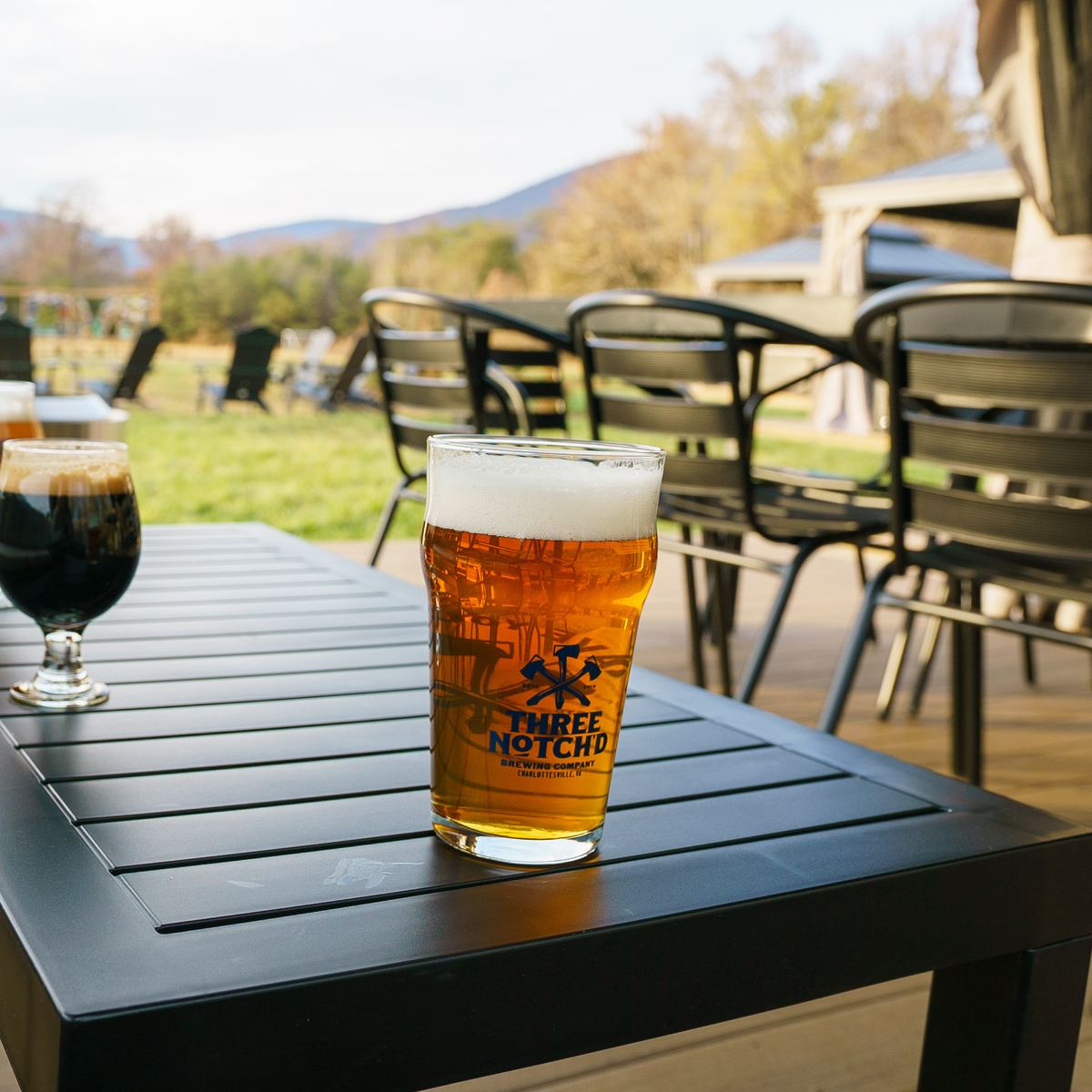 A Three Notch'd pint of amber beer on a patio table, mountains behind